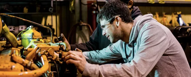 Students working on heavy equipment in a campus workshop.