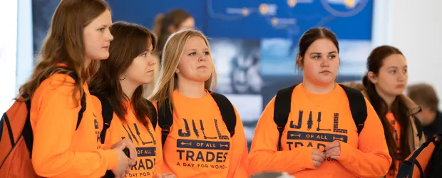 Students in orange “Jill of All Trades” shirts listening during a skilled trades event