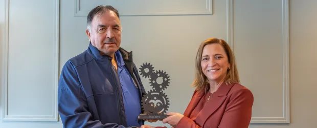 Two people shaking hands while holding an award plaque