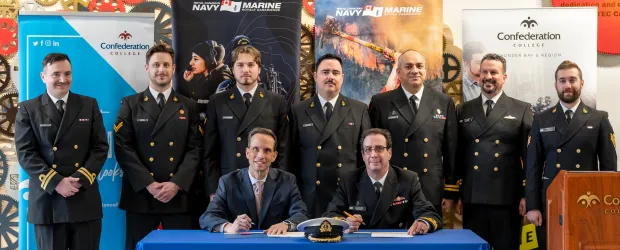 Royal Canadian Navy personnel and officials sign agreement at Confederation College with banners in background