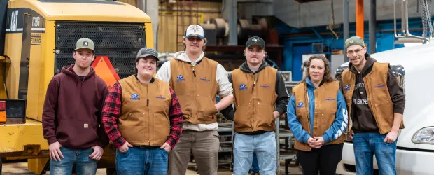 Trades students and instructors standing in an industrial workshop on campus.
