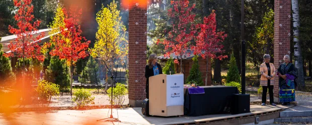 Speaker at Confederation College outdoor event stage surrounded by autumn trees and gathering space