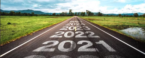 A country road with mountains in the distance.  The years 2021, 2022, 2021, 2024, 2025 are written on the road with 2025 the furthest in the distance, toward the mountains.
