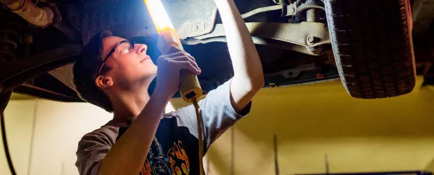 photo - Automotive student inspecting underside of a vehicle