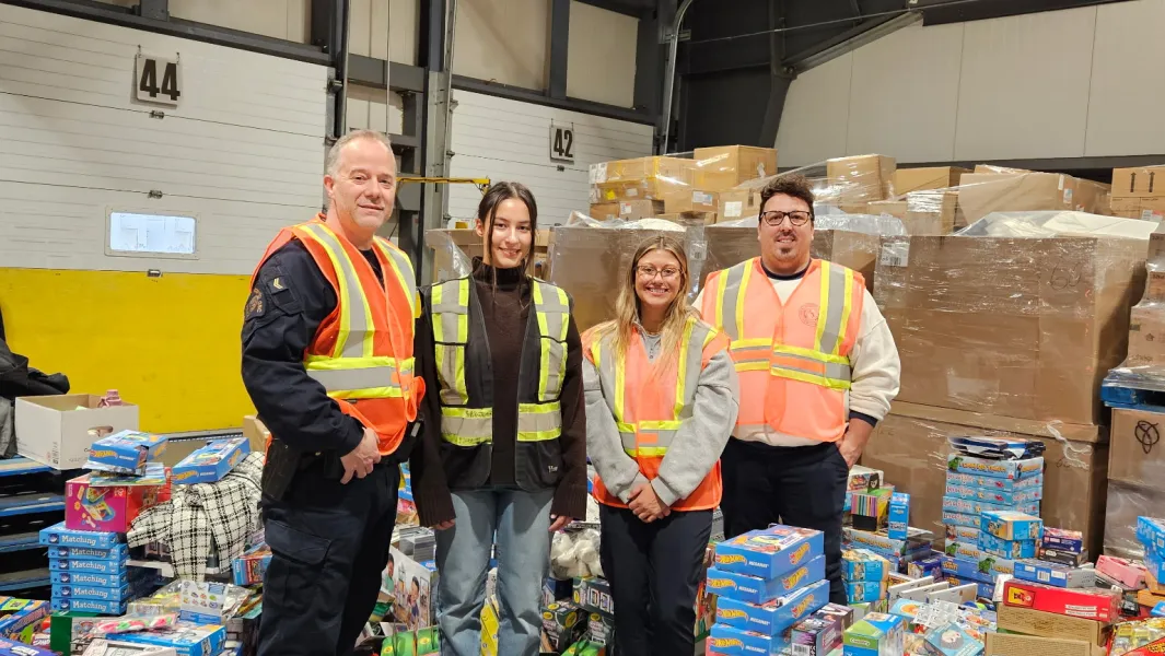 Volunteers wearing safety vests stand among donated toys and supplies in a warehouse.