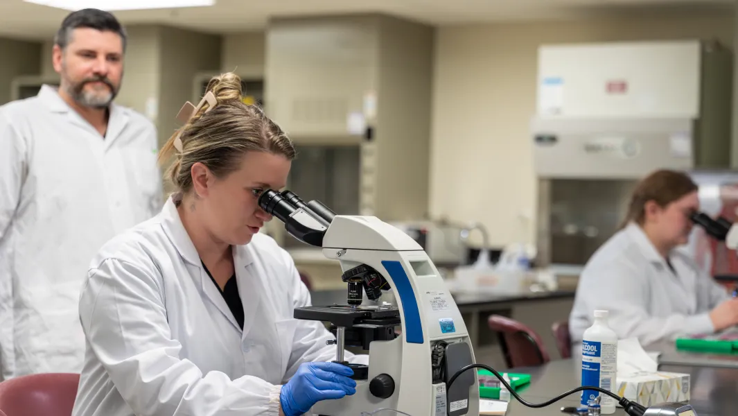 Students in lab coats examining samples with microscopes in a science laboratory.