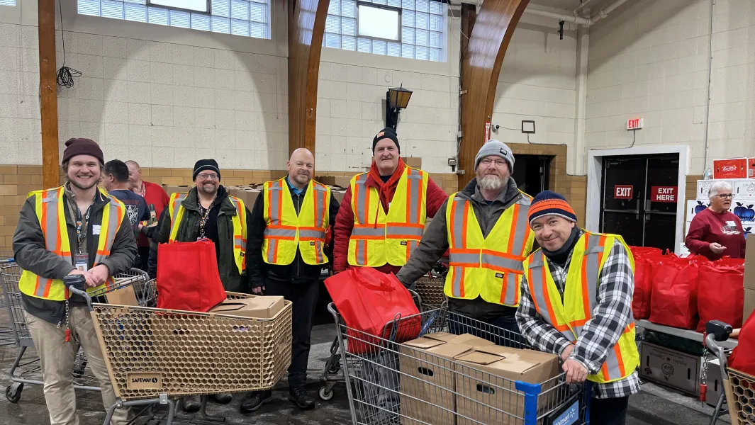 Volunteers wearing safety vests stand with carts of donated goods inside a community warehouse