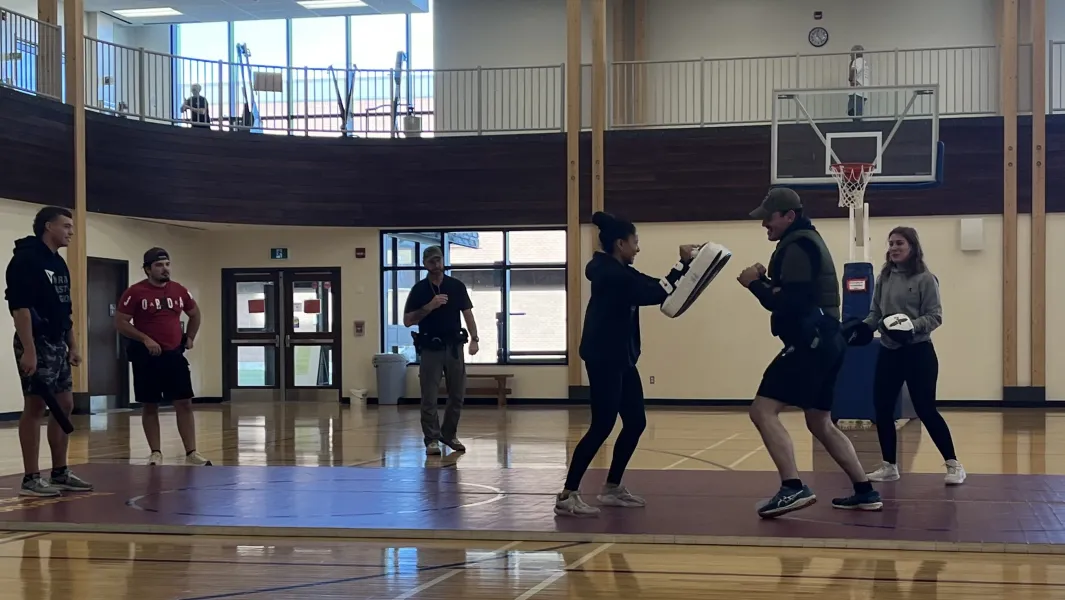 Students practice defensive tactics with pads in a gymnasium