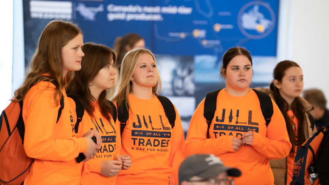 Students in orange “Jill of All Trades” shirts listening during a skilled trades event