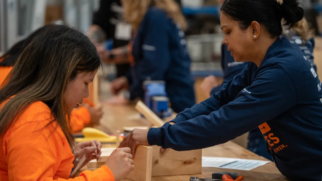 Participant helping a student assemble a small wood project during a hands-on trades workshop