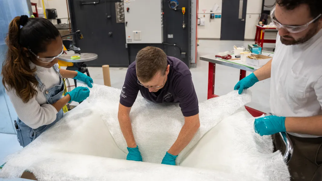 Students and instructor position fiberglass fabric in a mold during a hands-on composites manufacturing lab