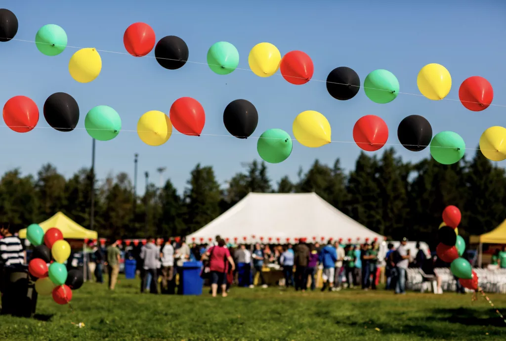 A group of people enjoying a sunny day on a green lawn with colorful balloons in the air