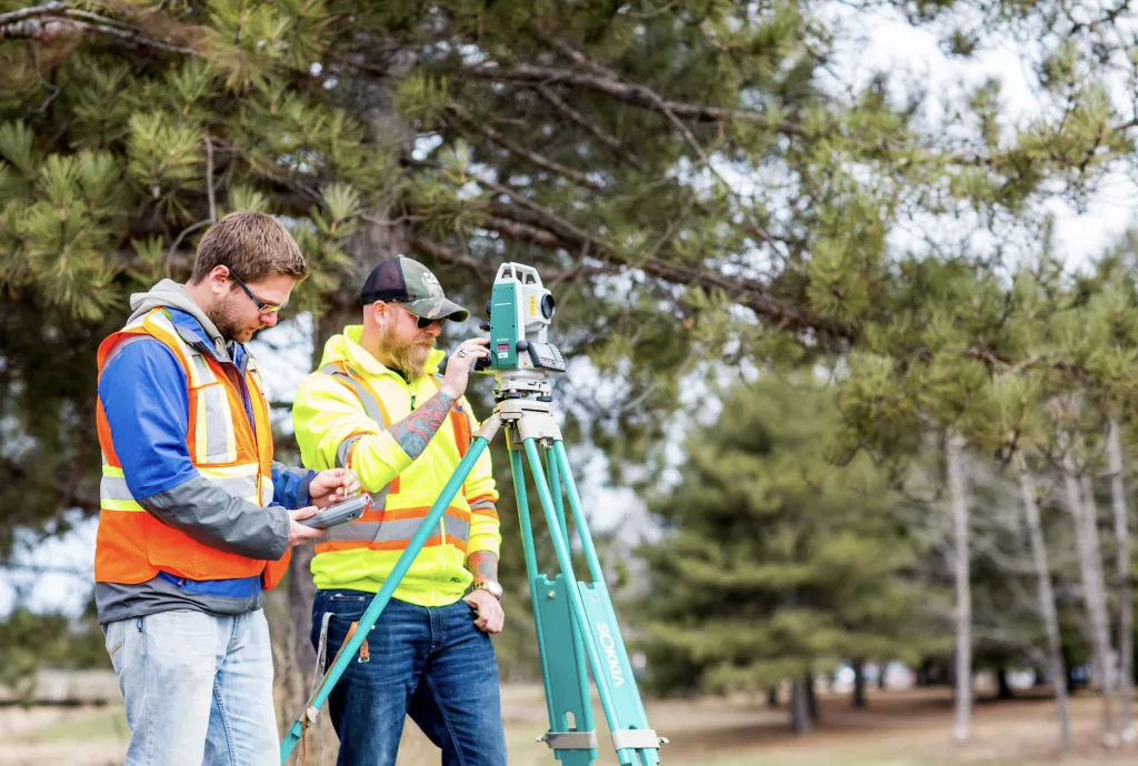 Two men in builder's clothes use a level measuring tool on a construction site as part of Facility Services at Confederation College