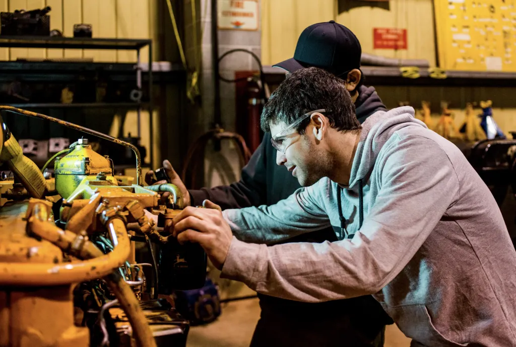Students working on heavy equipment in a campus workshop.