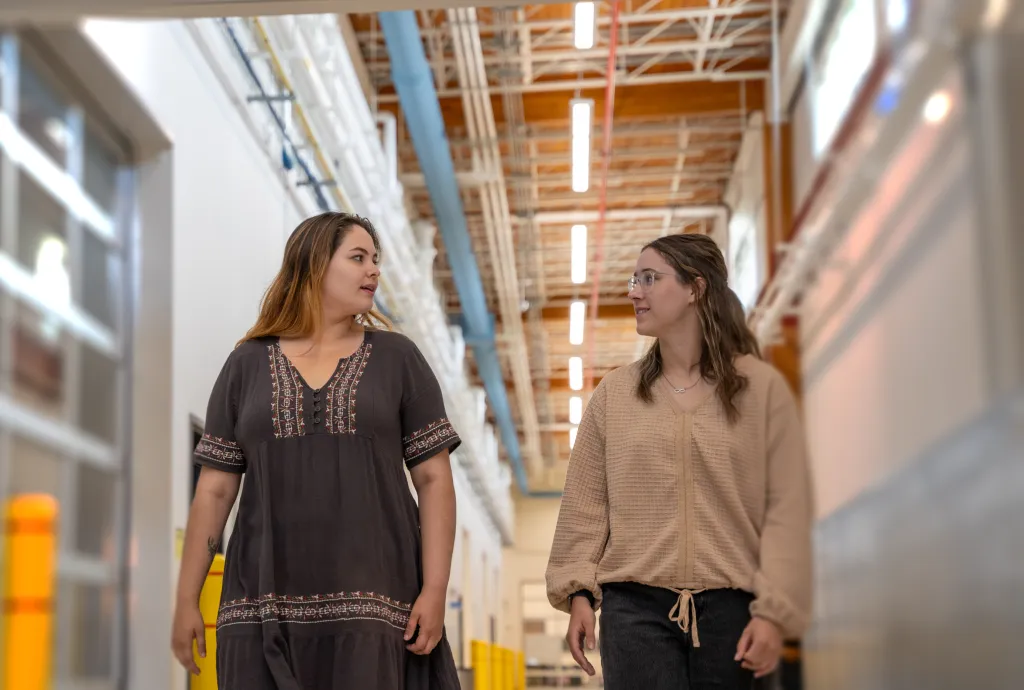 wo students walking and talking inside a bright hallway at Confederation College