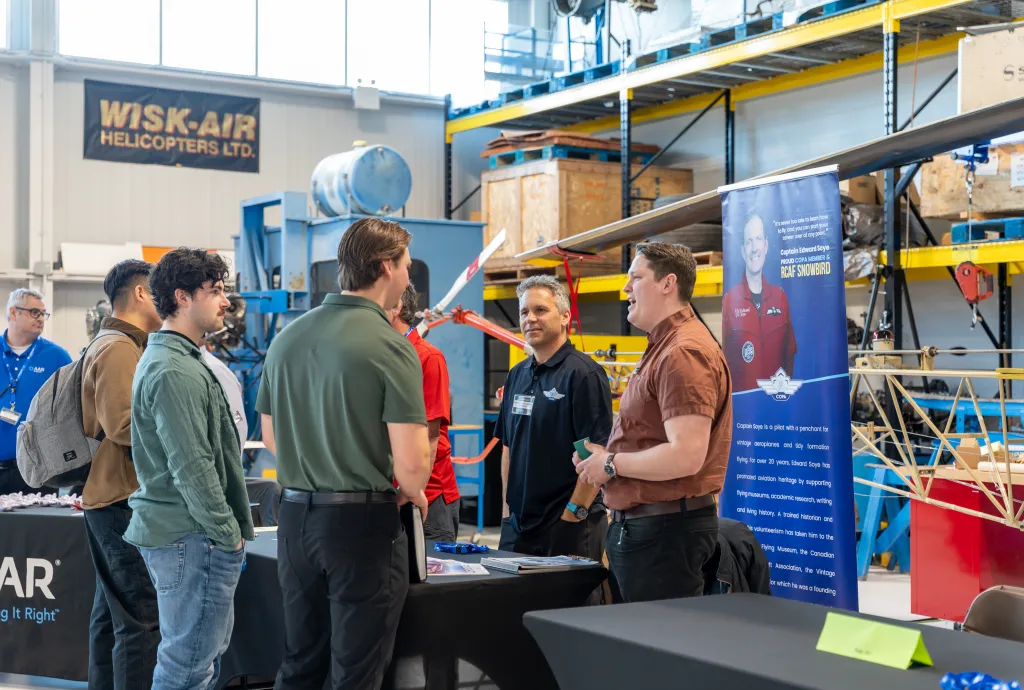 Students speak with aviation employers at Confederation College Aviation Day inside training hangar with aircraft equipment