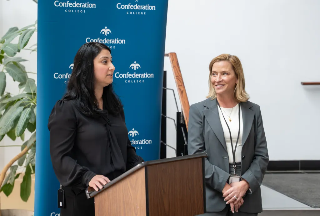 Two persons at podium during Confederation College announcement event with Alstom partnership backdrop.