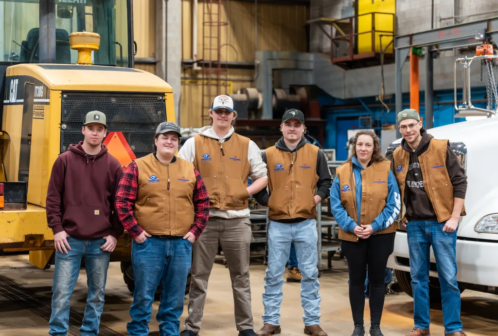 Trades students and instructors standing in an industrial workshop on campus.