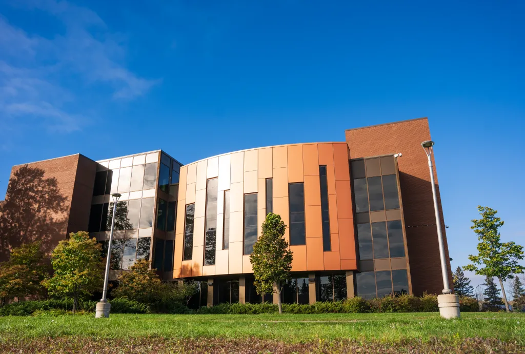 Exterior view of Shuniah Building with orange and brick facade, surrounded by greenery and a blue sky.