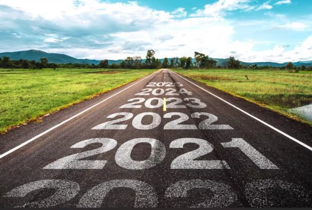 A country road with mountains in the distance.  The years 2021, 2022, 2021, 2024, 2025 are written on the road with 2025 the furthest in the distance, toward the mountains.