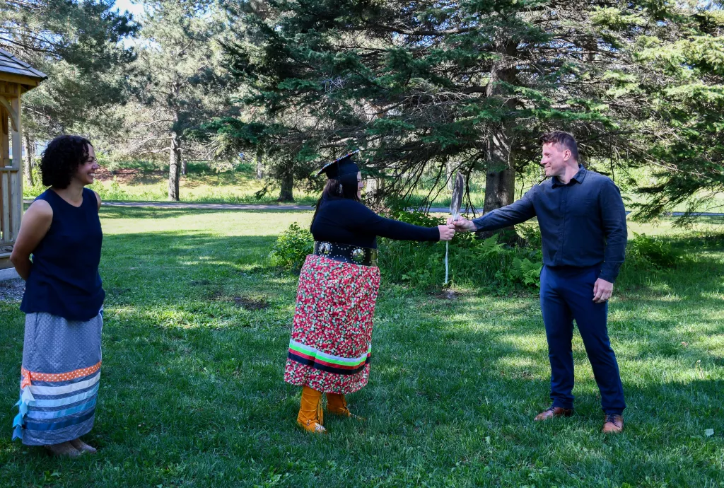 Program Coordinator Pam Burton looks on as alumna Courtney Forbes passes eagle feather to incoming student Derek Hrynczak to signify transition to Onajigawin Indigenous Services.