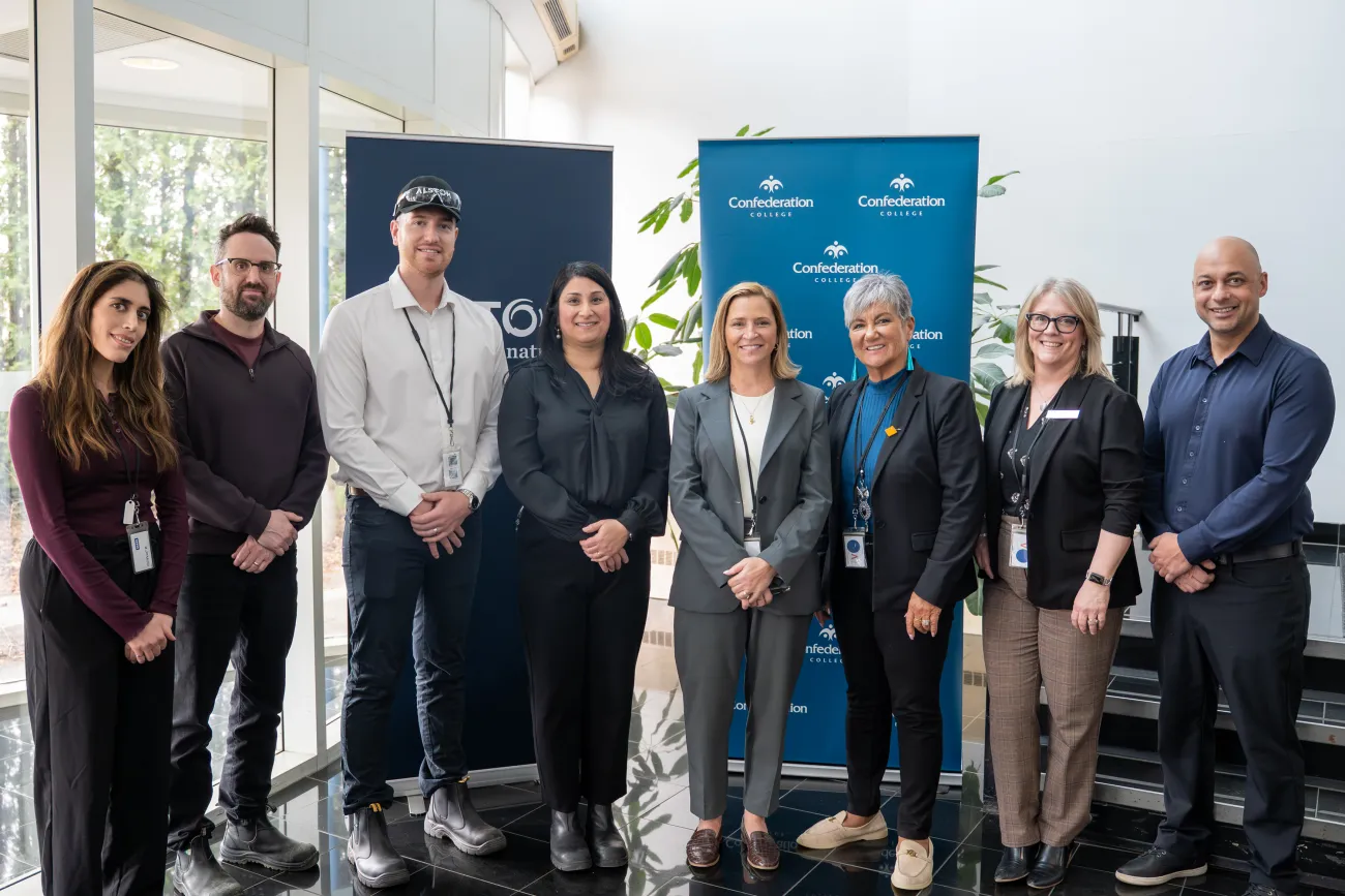 Group of persons posing indoors in front of Confederation College and Alstom banners during partnership announcement.