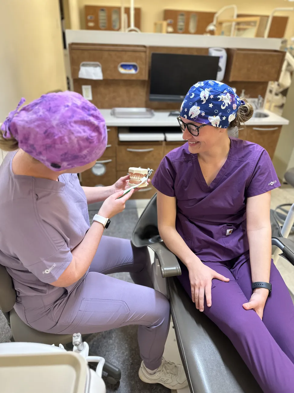 Dental hygiene student demonstrating brushing techniques with a dental model in a clinical training lab