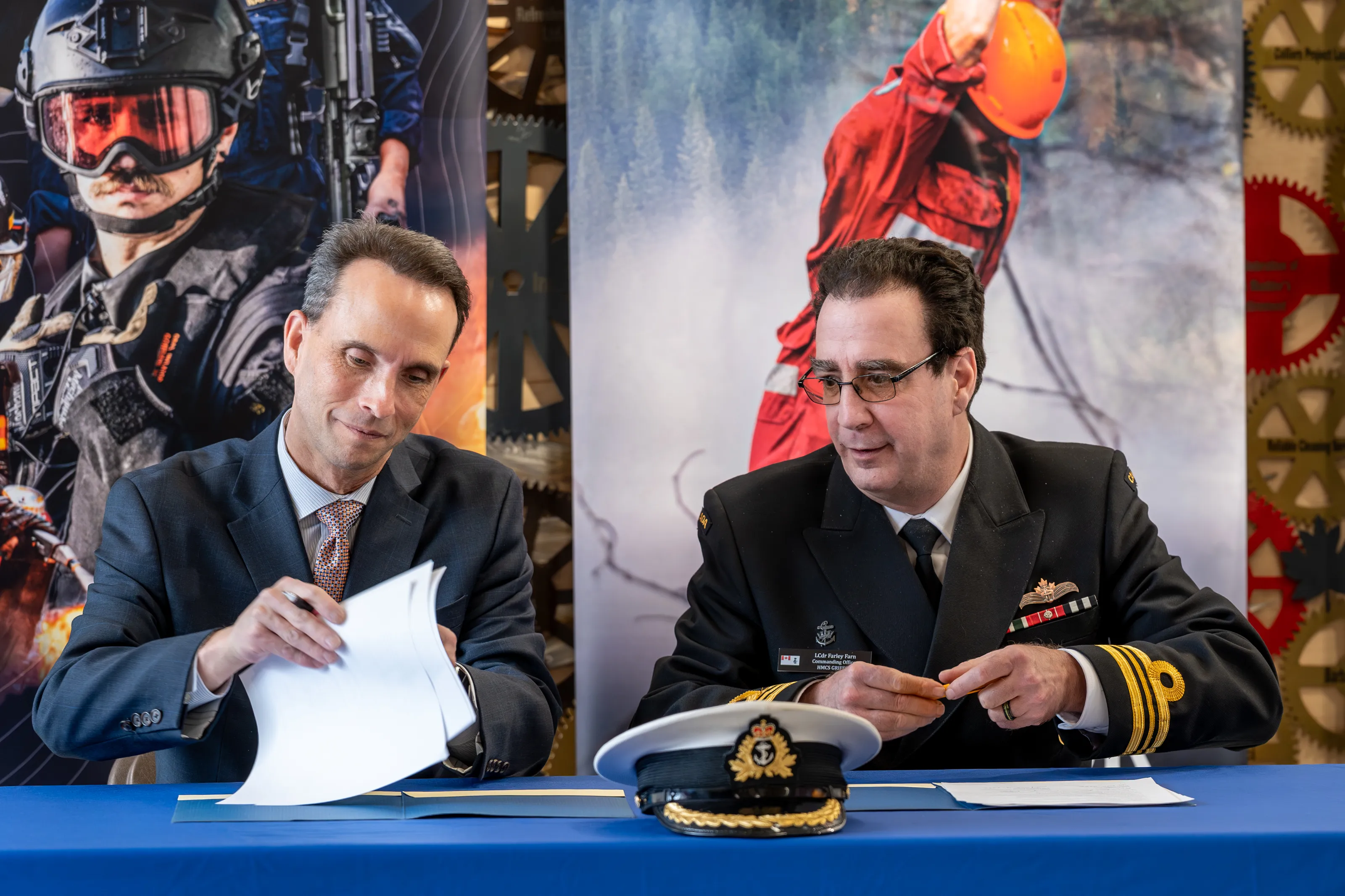 Two officials sign documents at a table during a Royal Canadian Navy partnership event at Confederation College.