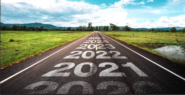 A country road with mountains in the distance.  The years 2021, 2022, 2021, 2024, 2025 are written on the road with 2025 the furthest in the distance, toward the mountains.